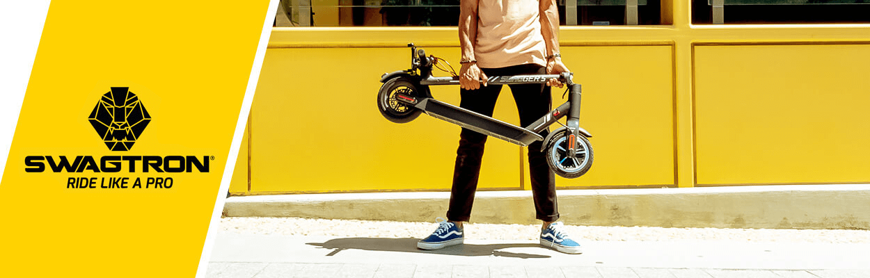 An adult holding a folded electric scooter on a city sidewalk.