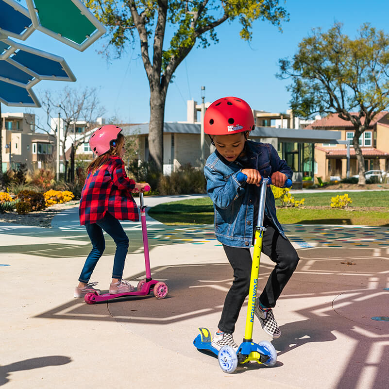 Boy and girl riding their three-wheel scooters at the park while having fun during playtime